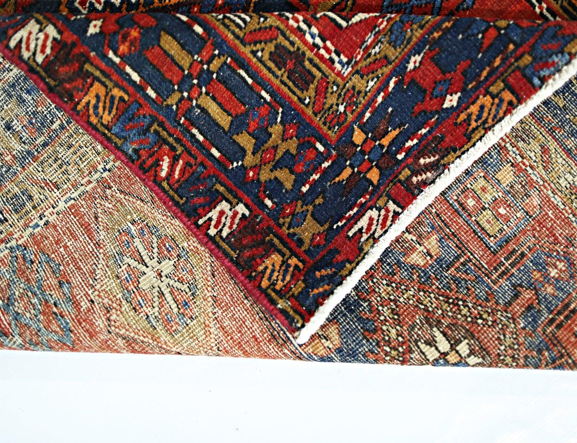A folded vintage Persian runner featuring intricate geometric patterns in red, blue, and tan.