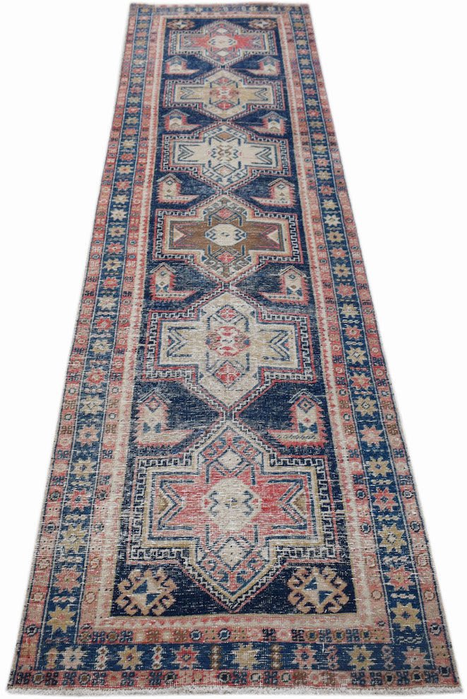 A handwoven vintage Persian runner featuring geometric medallions in blue, red, and beige tones.