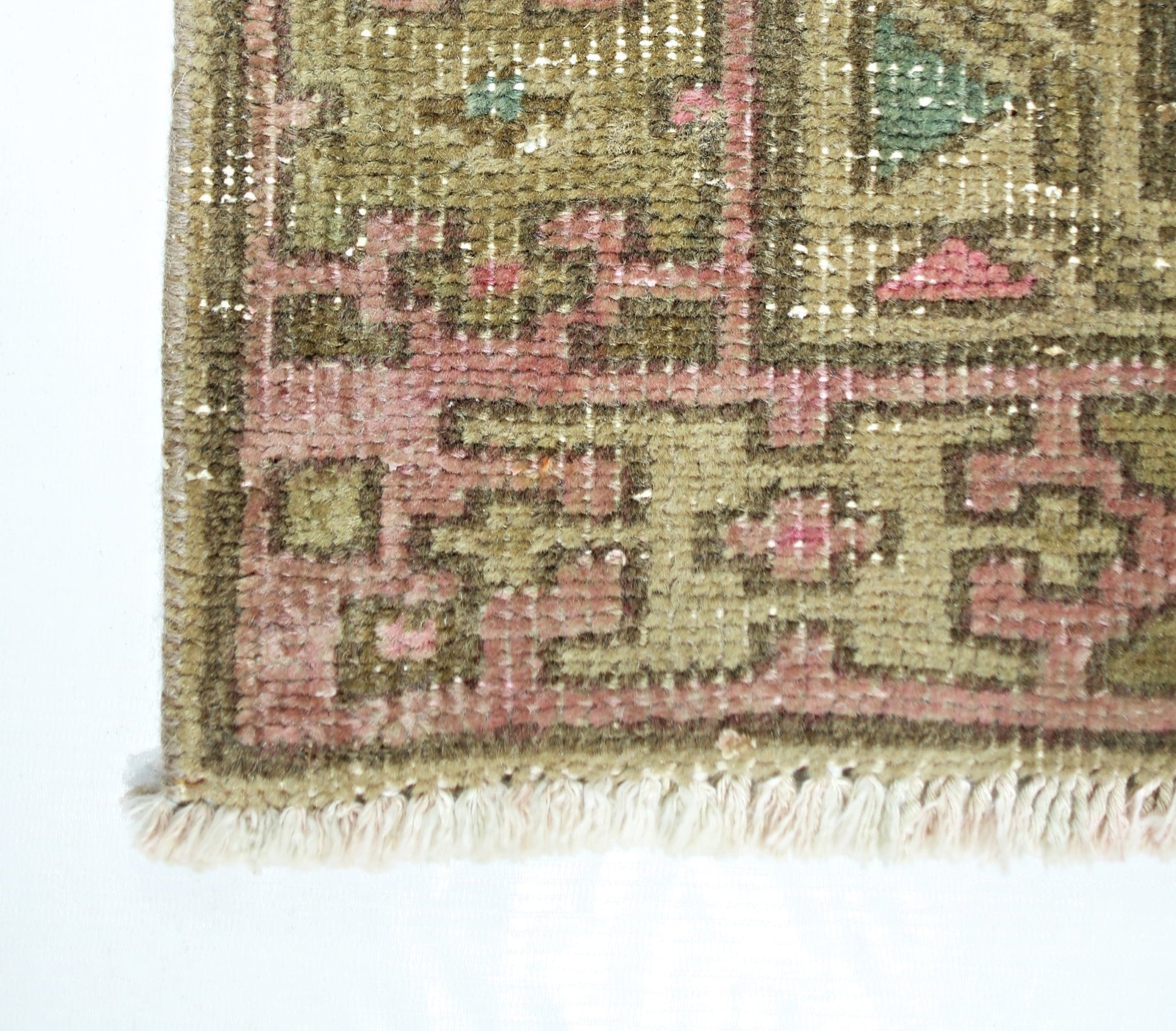 A close-up of a vintage Persian runner featuring a geometric pattern in olive green and pink.