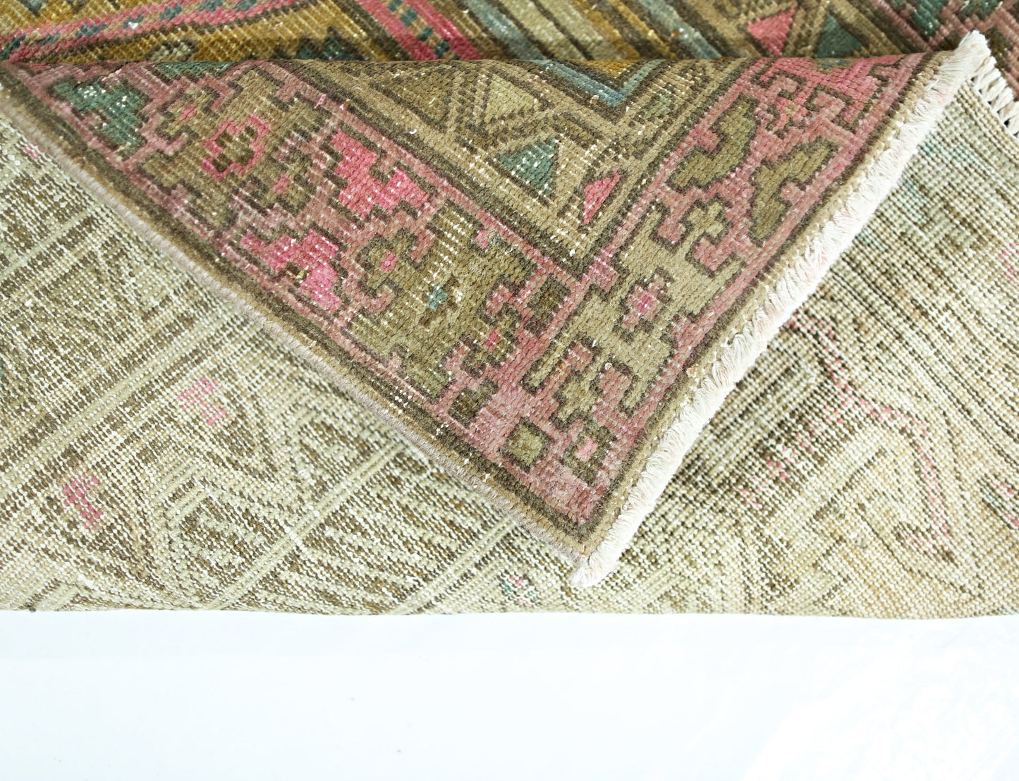 A folded vintage Persian runner featuring a geometric pattern in muted green, pink, and brown tones.