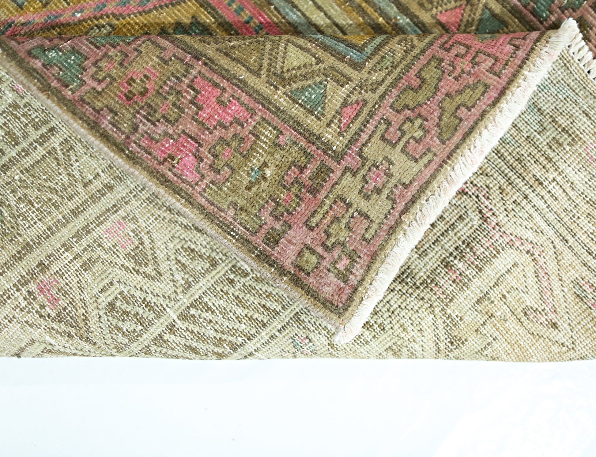 A folded vintage Persian runner featuring a geometric pattern in muted green, pink, and brown tones.