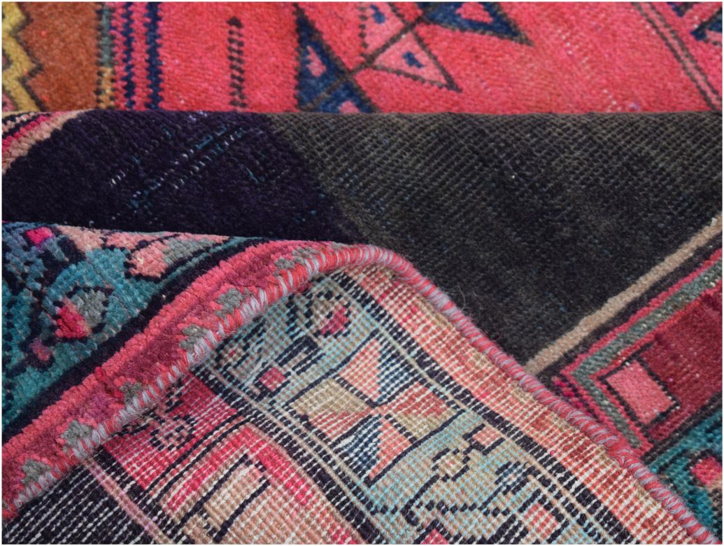A folded vintage Persian Hamadan runner featuring intricate geometric patterns in pink and blue.
