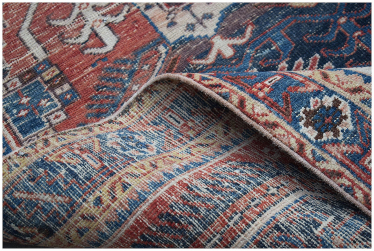 A vintage Persian Hamadan rug with a folded corner showing intricate blue and red floral patterns.