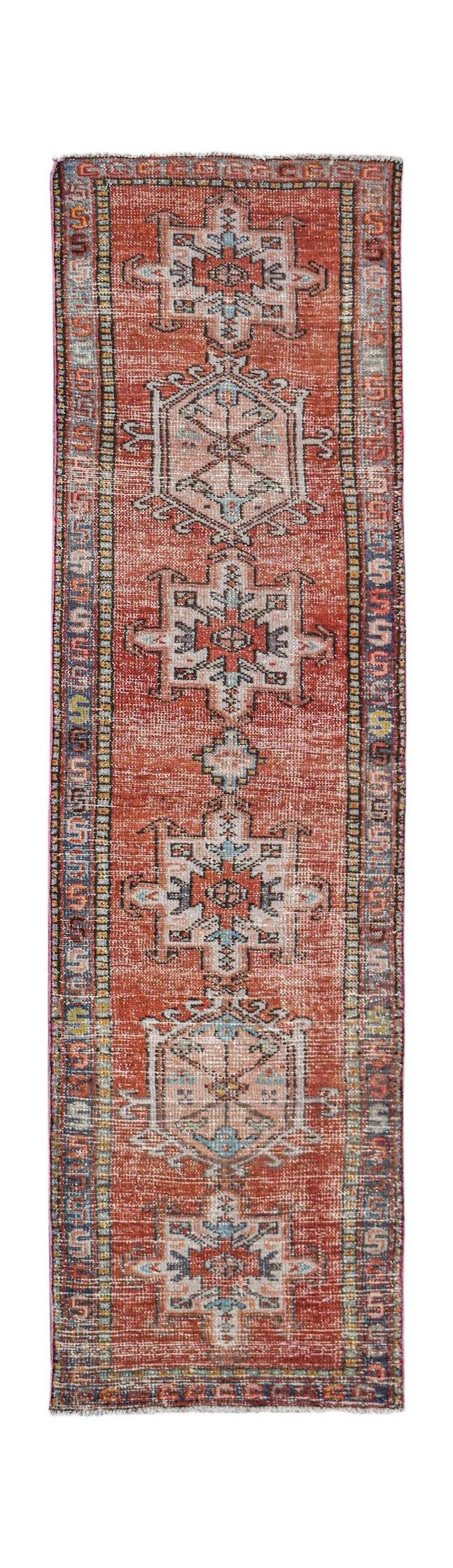 A vintage handwoven Persian Karaja runner featuring geometric medallions on a rust red field.