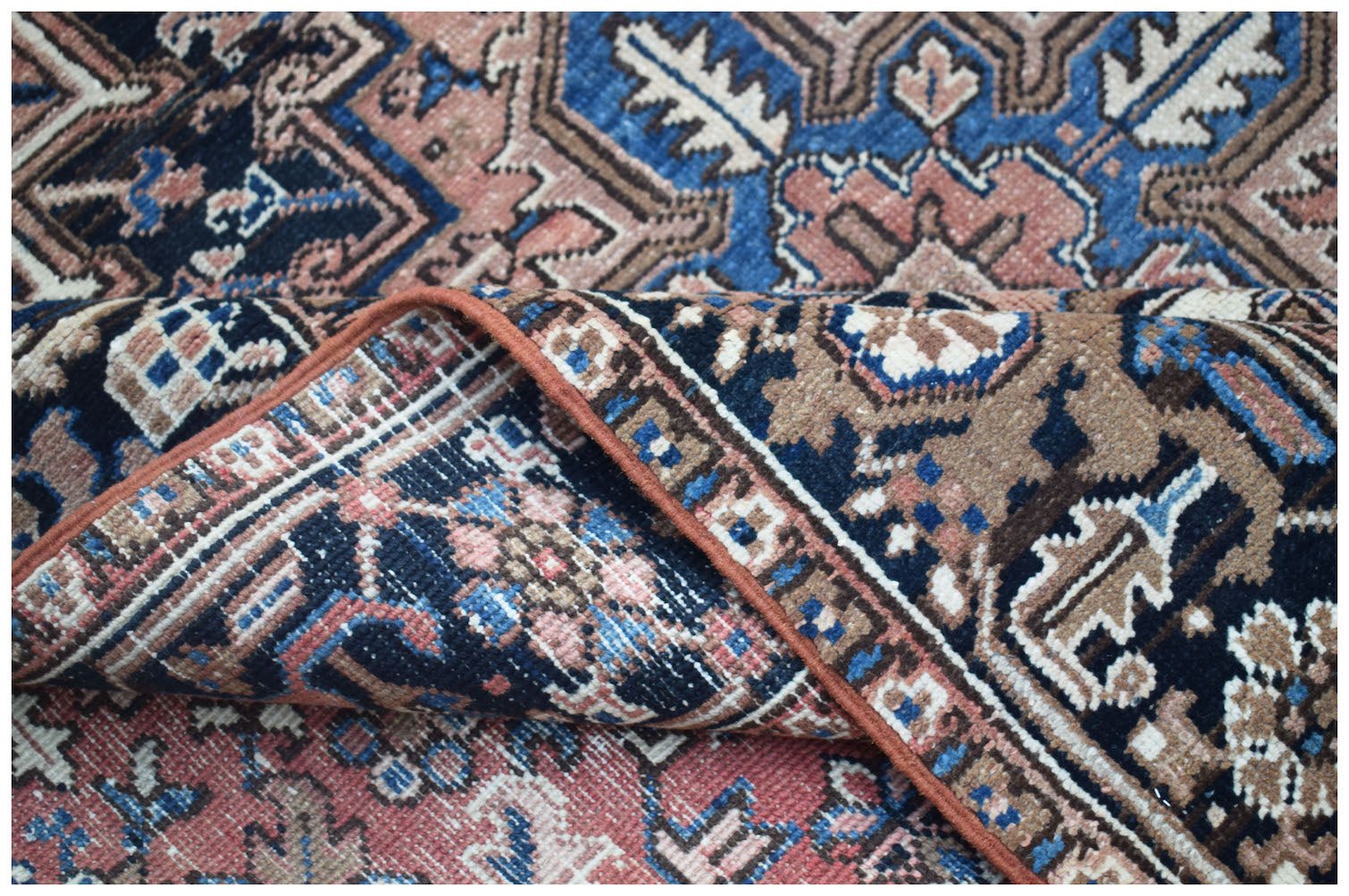 A vintage Persian Heriz rug featuring a geometric floral pattern in blue, pink, and brown tones.