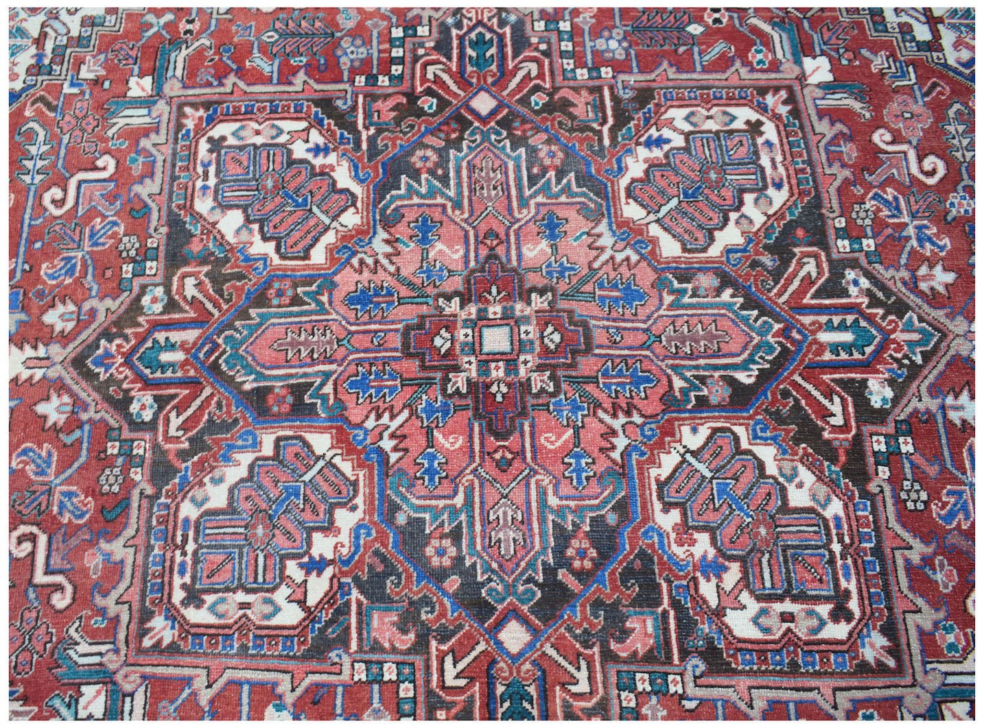A vintage handwoven Persian Heriz rug featuring a geometric medallion in red, blue, and cream.