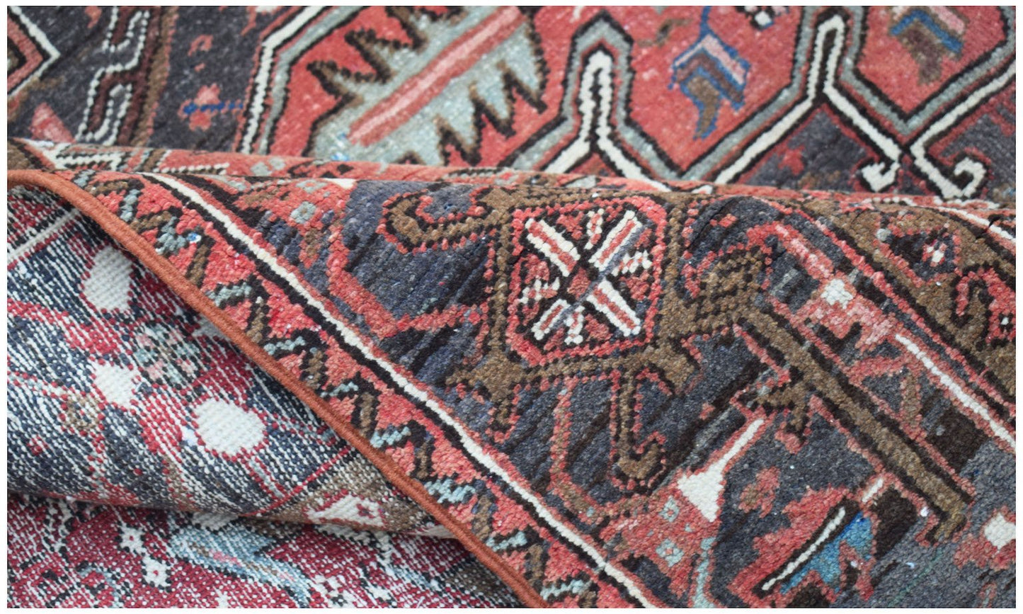 A folded vintage Persian Heriz rug featuring intricate geometric patterns in red, blue, and brown.
