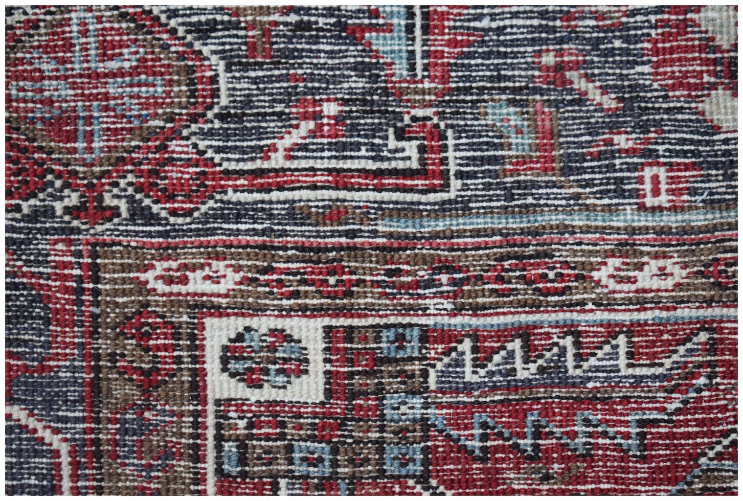 A close-up of a vintage Persian Heriz rug featuring intricate geometric patterns in red and blue.