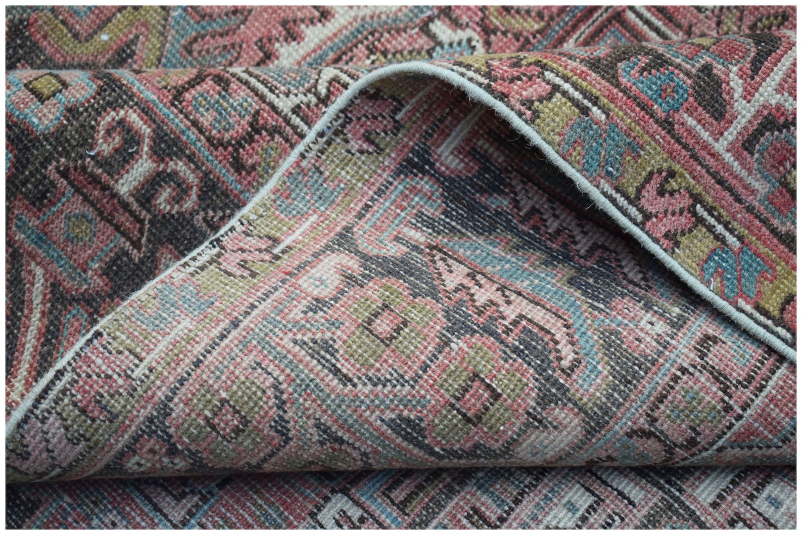 A folded vintage Persian Heriz rug featuring a geometric floral pattern in muted pink and blue.