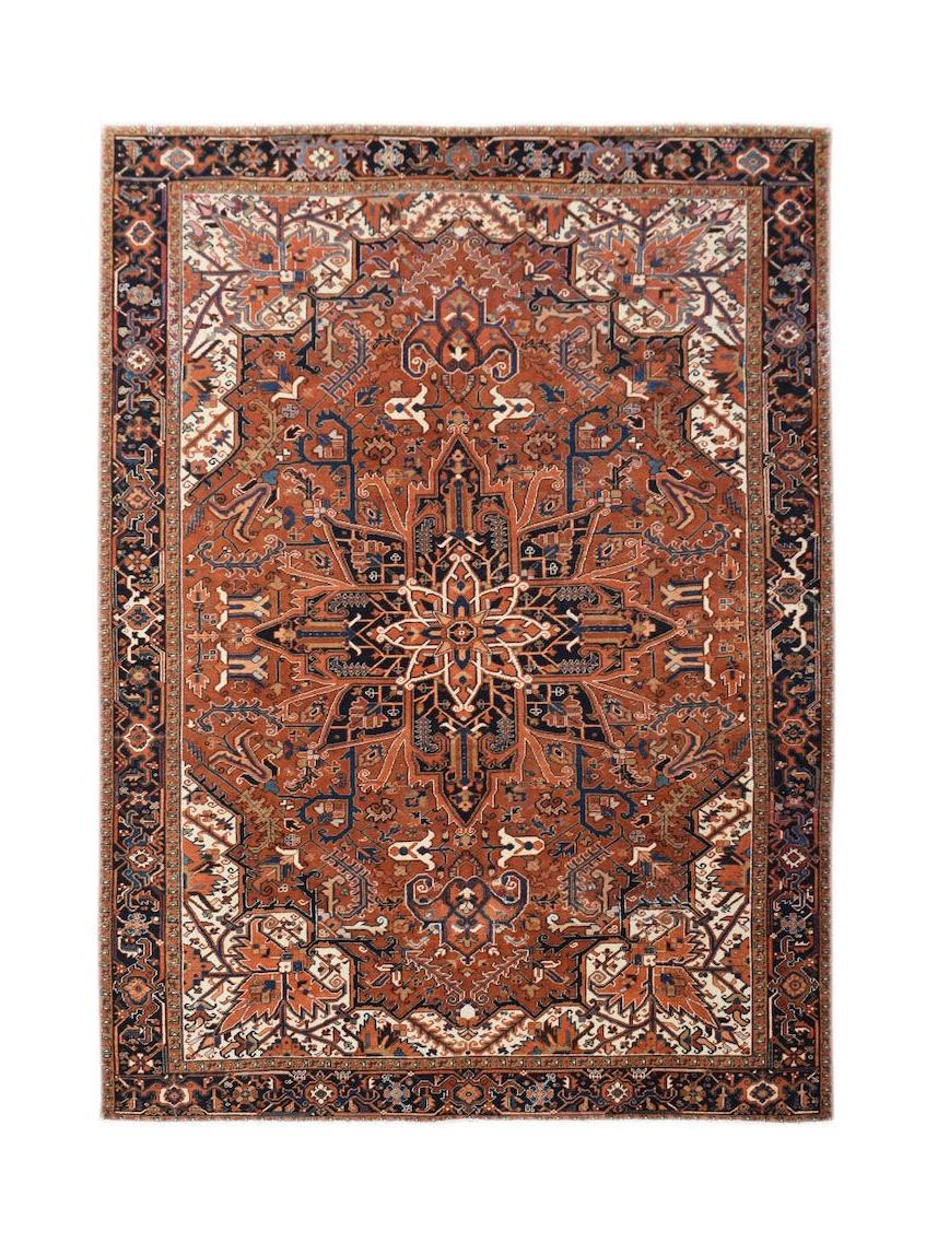 A vintage Persian Heriz rug featuring a geometric medallion on a rust-red field with navy borders.