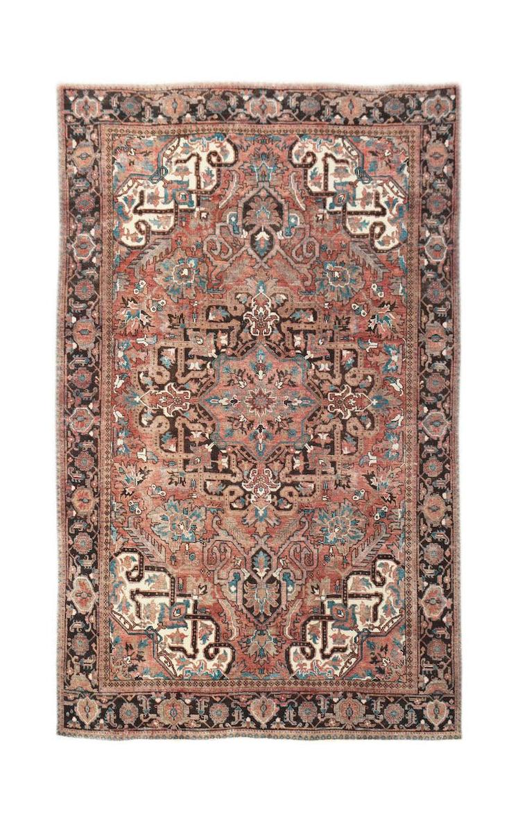 A vintage handwoven Persian Heriz rug featuring a geometric medallion in rust, blue, and cream.