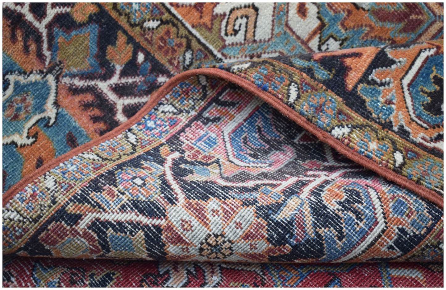 A folded vintage Persian Heriz rug featuring intricate floral patterns in blue, orange, and cream.