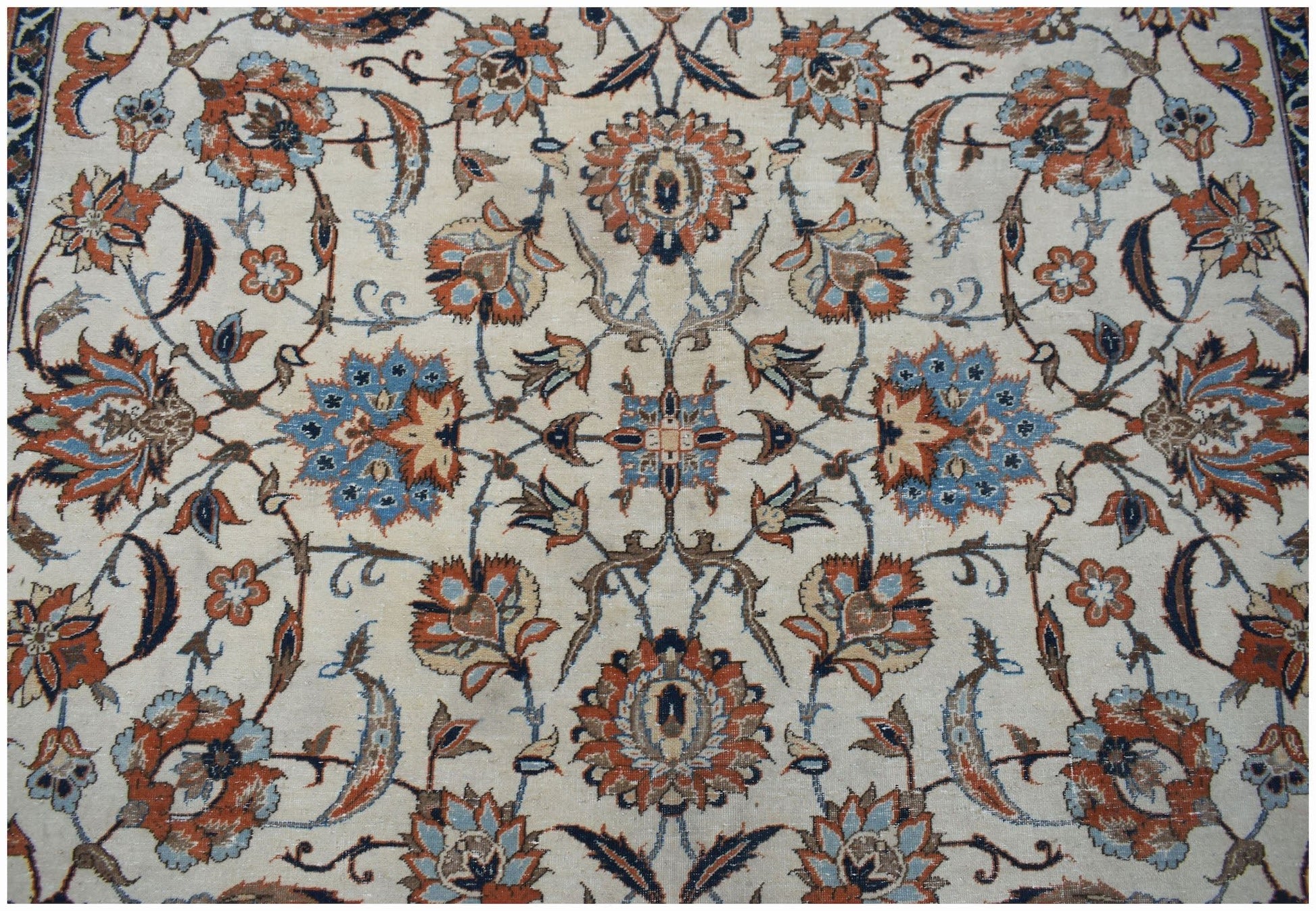 A vintage Persian Kashan rug featuring intricate floral patterns in blue, orange, and cream tones.