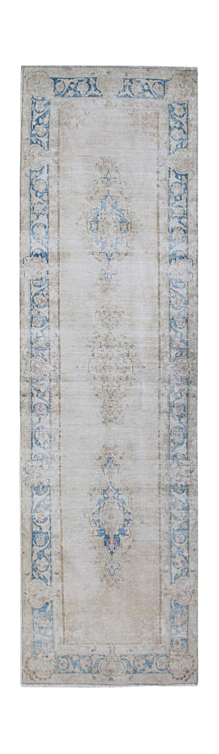 A vintage Persian Kerman runner rug featuring a central floral medallion on a light beige field.