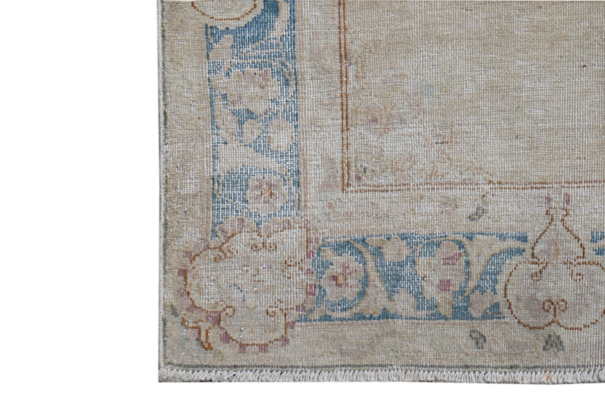 A close-up of a vintage Persian Kerman runner featuring a floral blue border on a beige field.