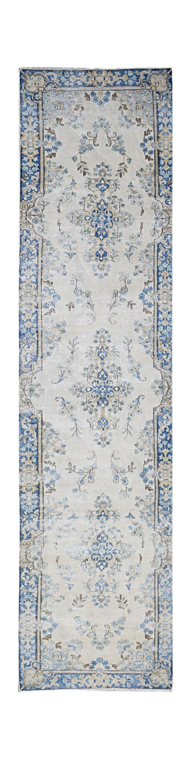 A vintage Persian Kerman runner rug featuring a blue floral medallion pattern on a cream background.