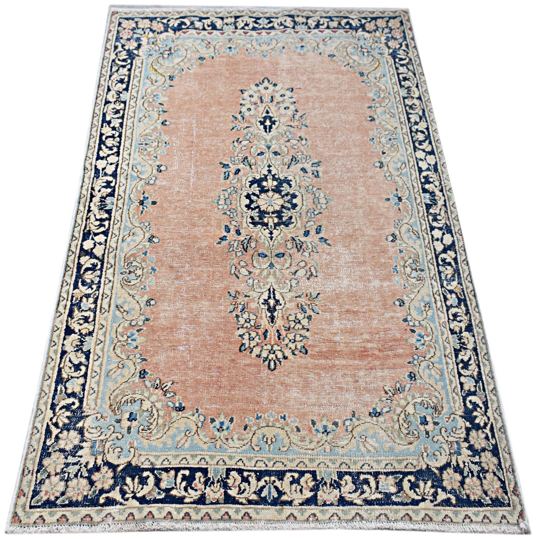 A vintage Persian Kerman rug featuring a central floral medallion on a soft peach field.