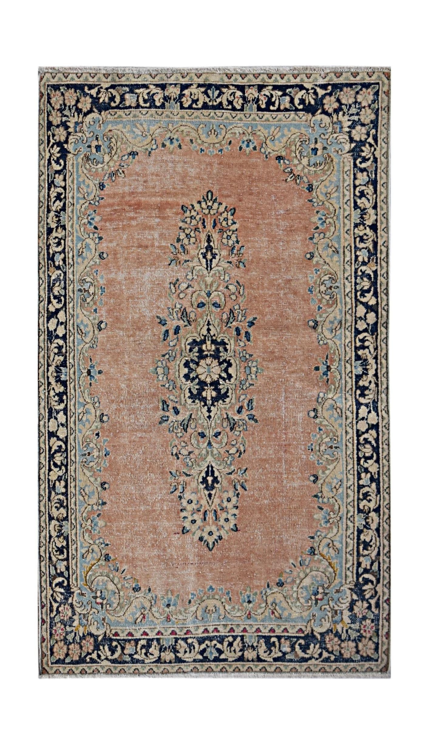 A vintage Persian Kerman rug featuring a central floral medallion on a soft peach field.