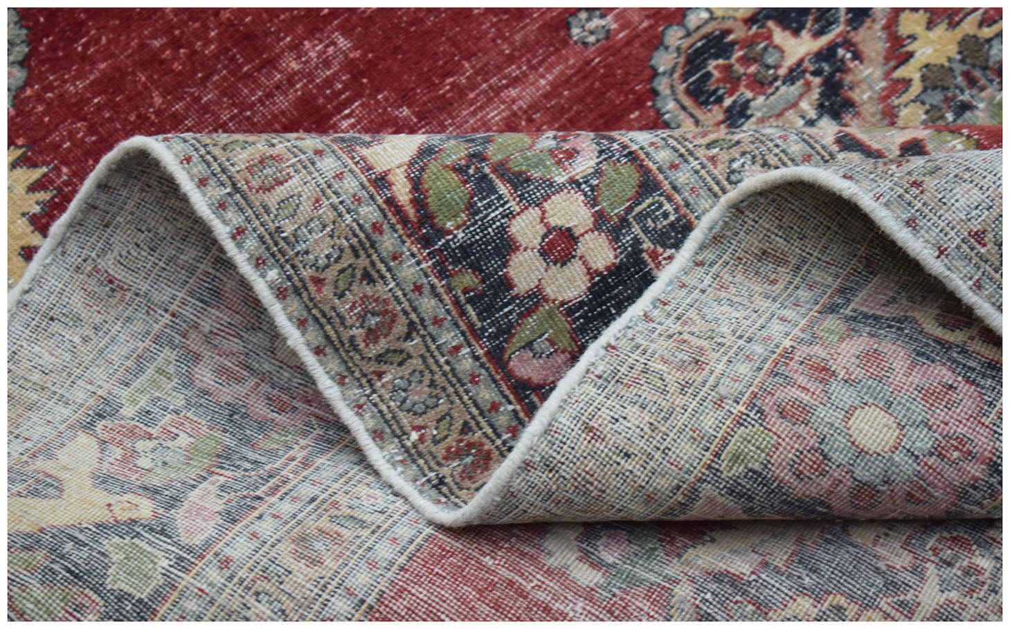A folded vintage Persian Kerman rug featuring a red field and intricate floral medallion patterns.