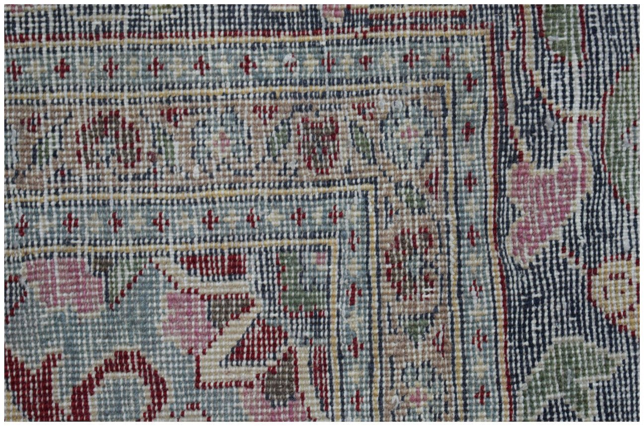 A close-up of a vintage Persian Kerman rug featuring intricate floral patterns and a blue border.