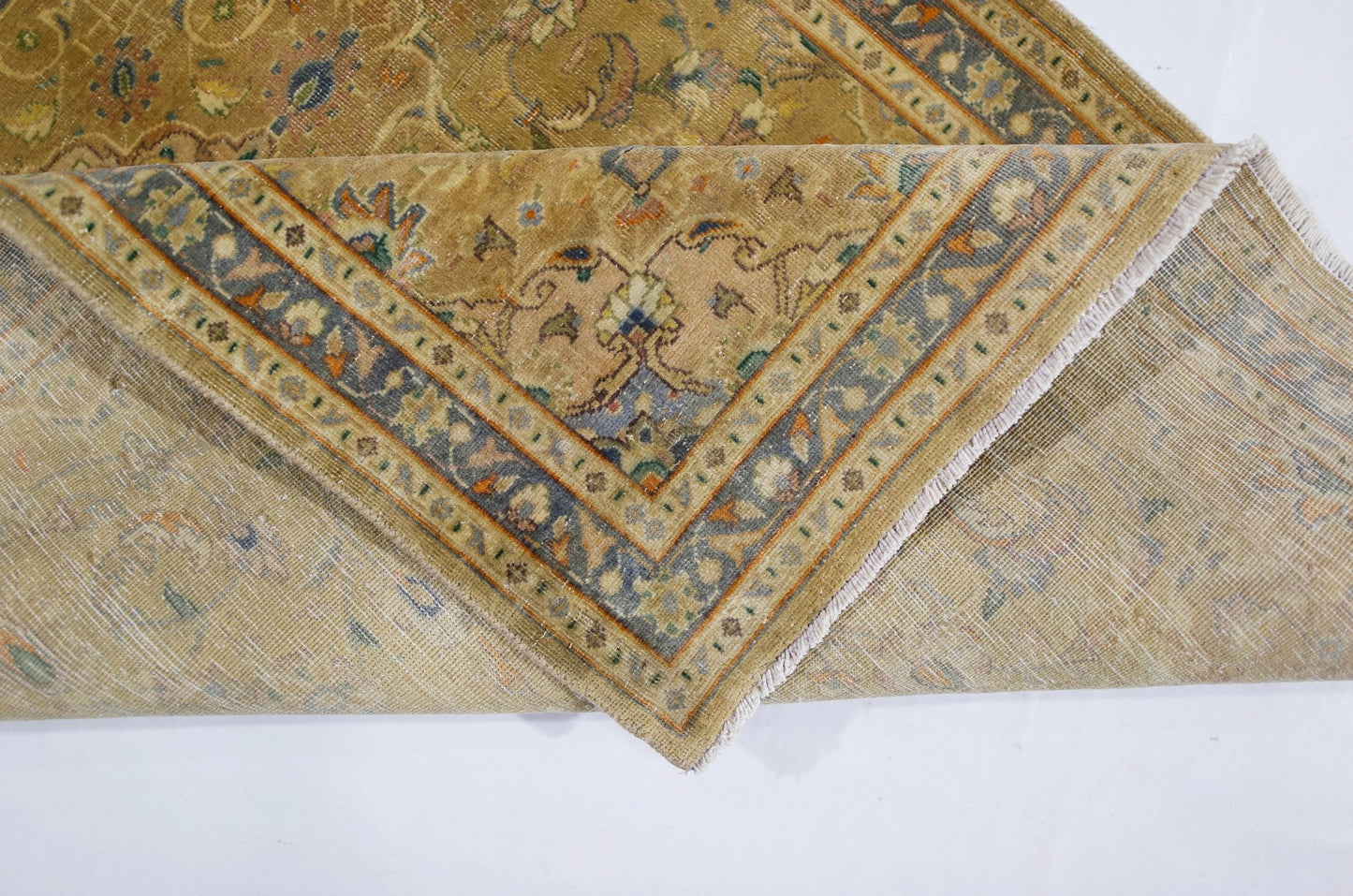 A vintage Pakistani rug with a folded corner revealing its intricate floral pattern and weave.