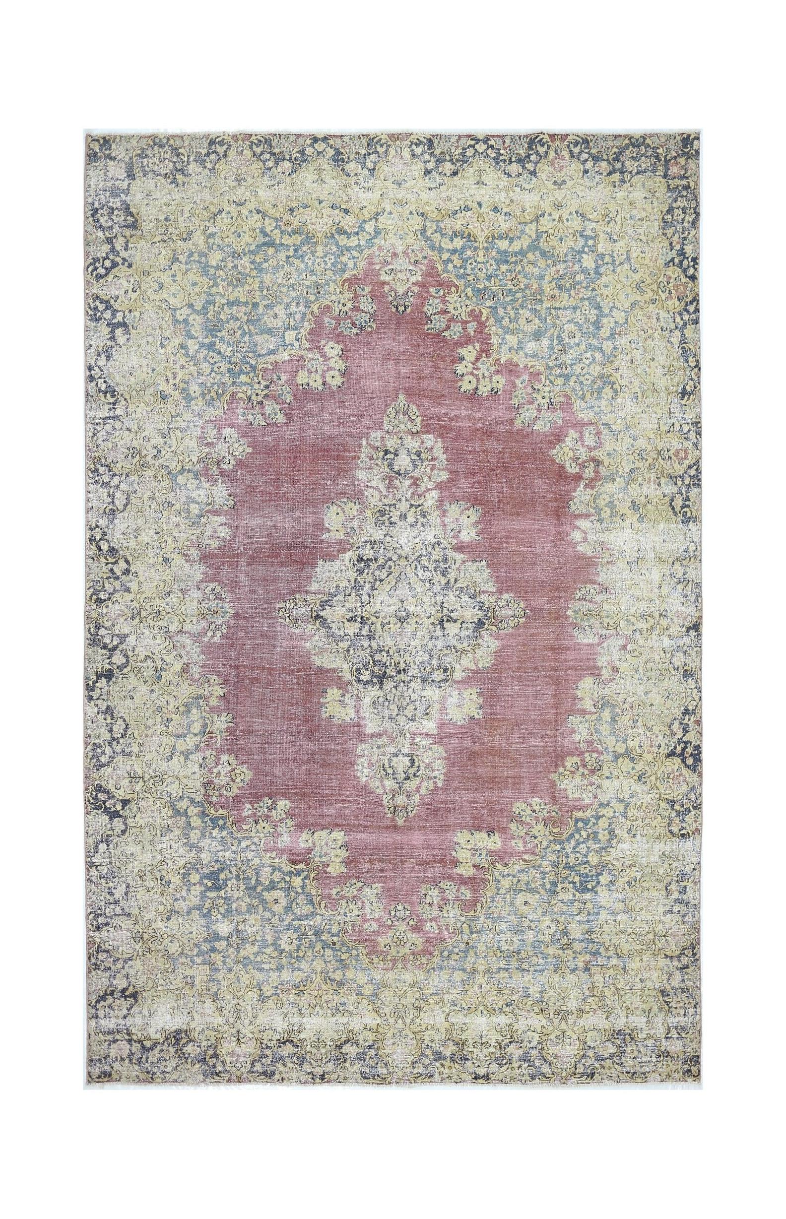 A vintage Persian Kerman rug featuring a central floral medallion in muted pink and blue tones.
