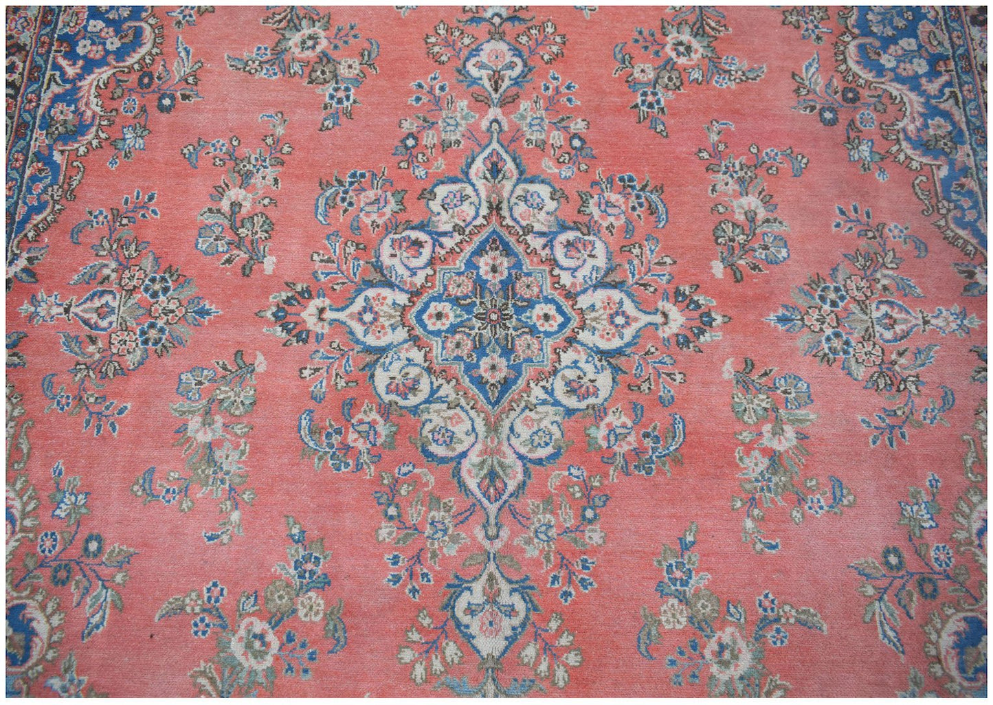 A vintage Persian Kerman rug featuring a central blue floral medallion on a coral field.