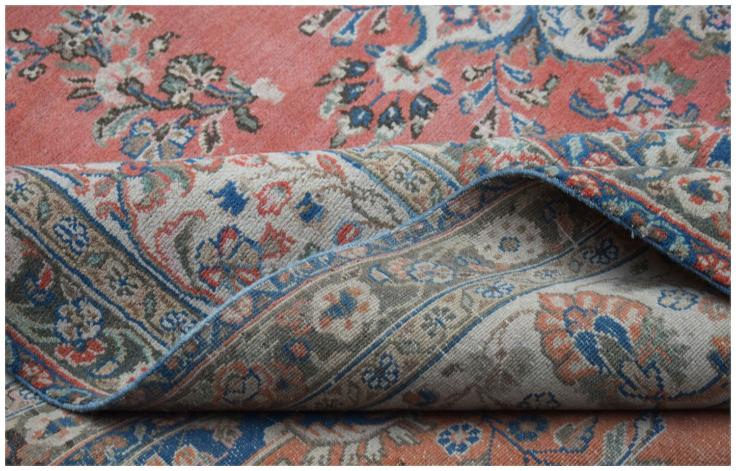 A vintage Persian Kerman rug featuring a floral pattern in shades of coral, blue, and cream.
