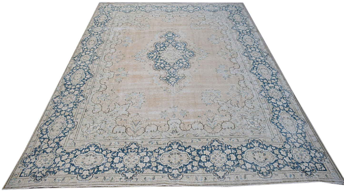 A vintage Persian Kerman rug featuring a central blue medallion on a soft beige floral field.