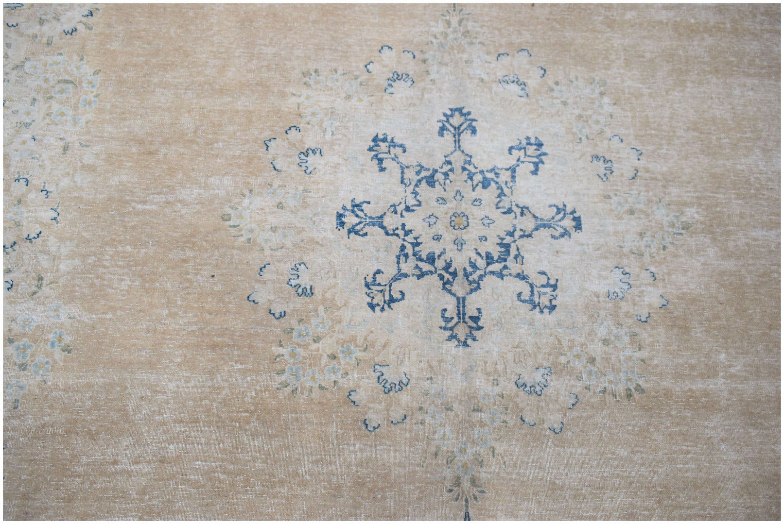 A vintage Persian Kerman rug featuring a central blue floral medallion on a beige field.