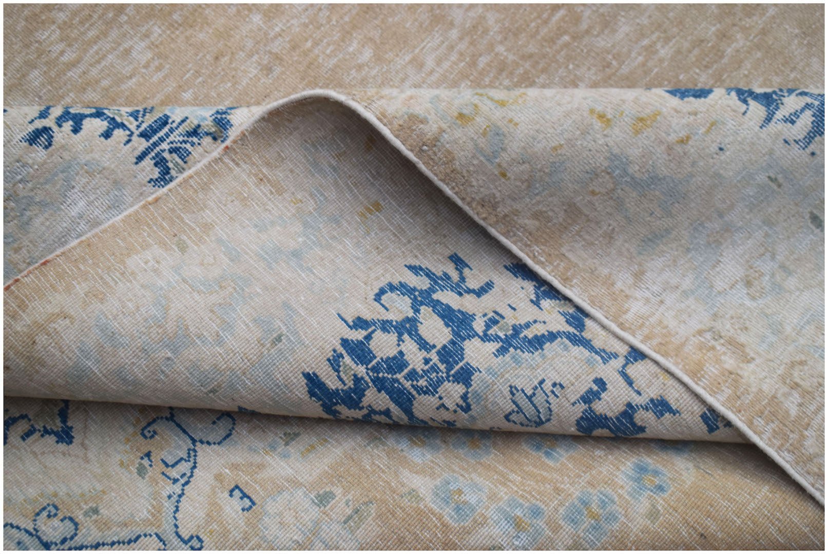 A vintage Persian Kerman rug with a beige background and intricate blue floral patterns.