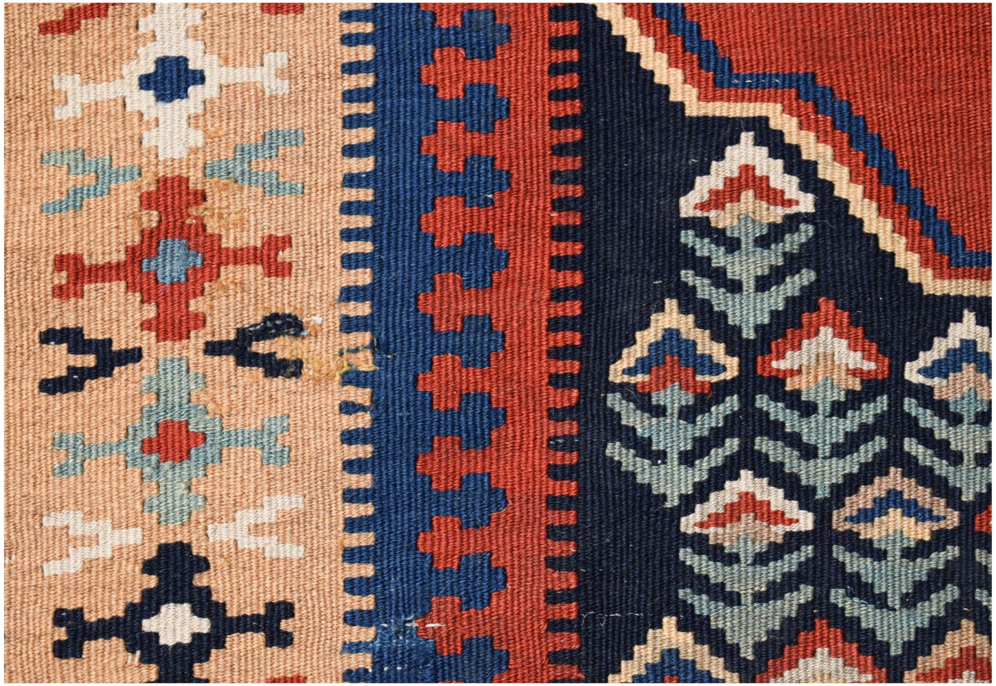A close-up of a handmade Persian kilim featuring geometric patterns in red, blue, and beige wool.