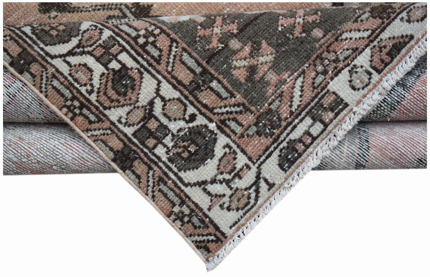 A folded vintage Persian Mazlaghan rug featuring a geometric pattern in muted pink and brown tones.