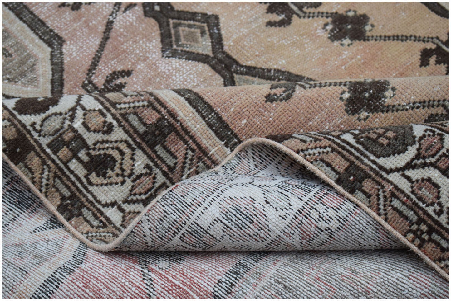 A vintage Persian Mazlaghan rug with a faded geometric pattern in muted pink and brown tones.