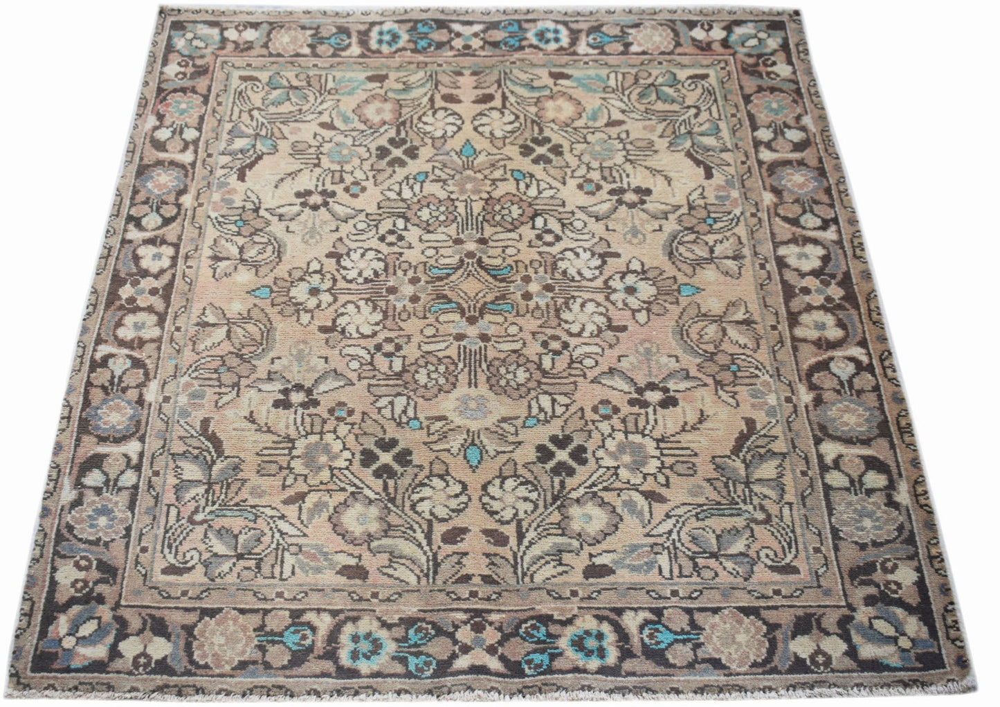 A vintage handwoven Persian rug featuring a floral pattern in muted tones on a beige background.