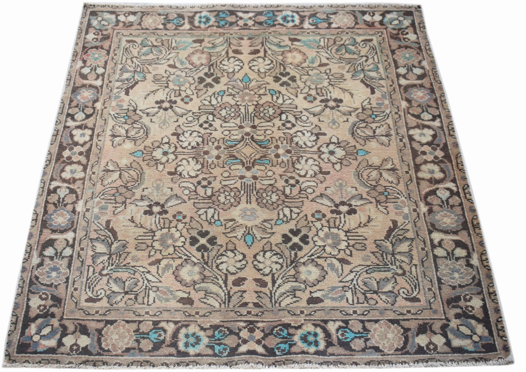 A vintage handwoven Persian rug featuring a floral pattern in muted tones on a beige background.