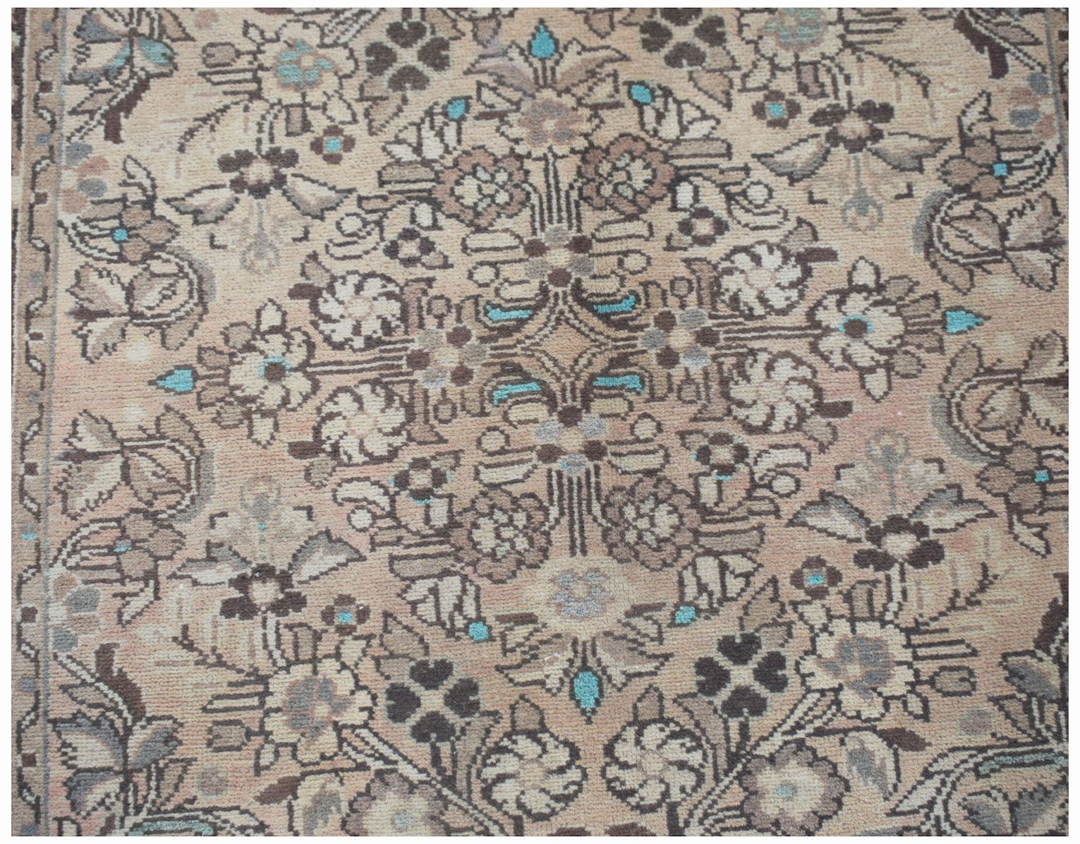 A vintage handwoven Persian rug featuring a floral pattern in muted tones with turquoise accents.