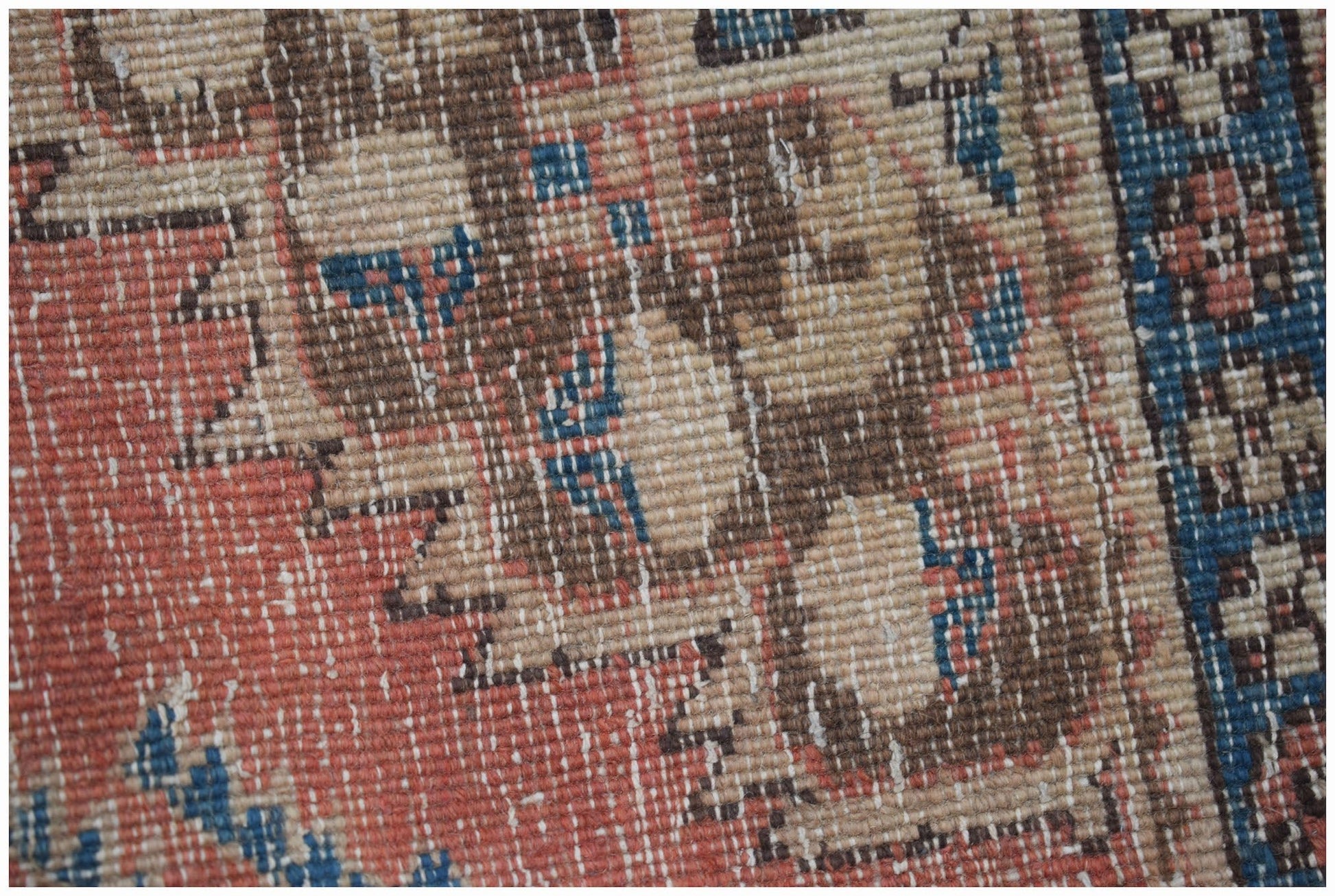 A close-up view of a handwoven vintage Persian rug featuring a faded geometric pattern in wool.