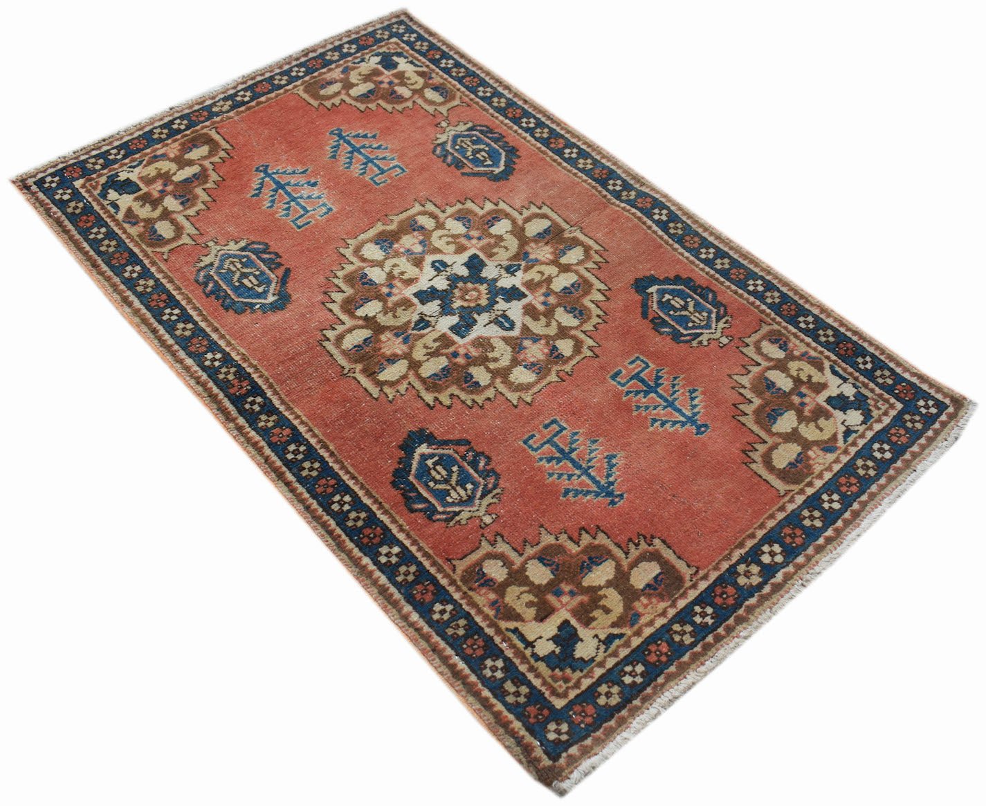 A vintage handwoven Persian rug featuring a central floral medallion on a faded red field.