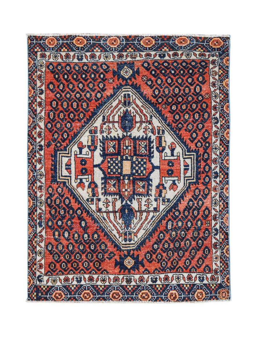 A handwoven vintage Persian rug featuring a central diamond medallion on a red and blue field.