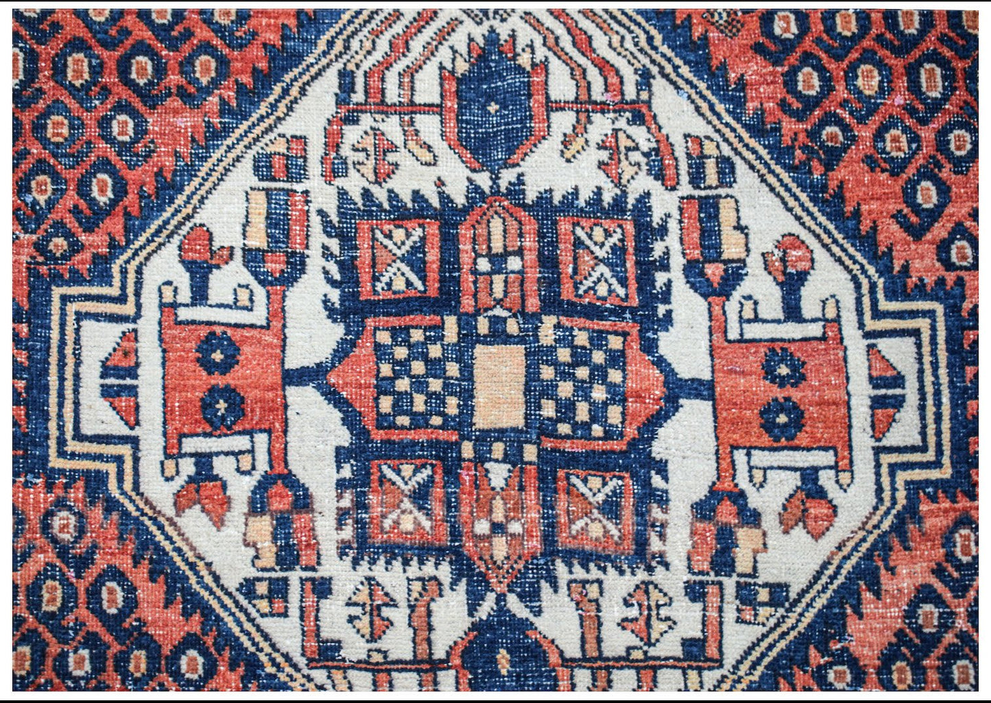 A vintage handwoven Persian rug featuring a geometric central medallion in red, blue, and cream.