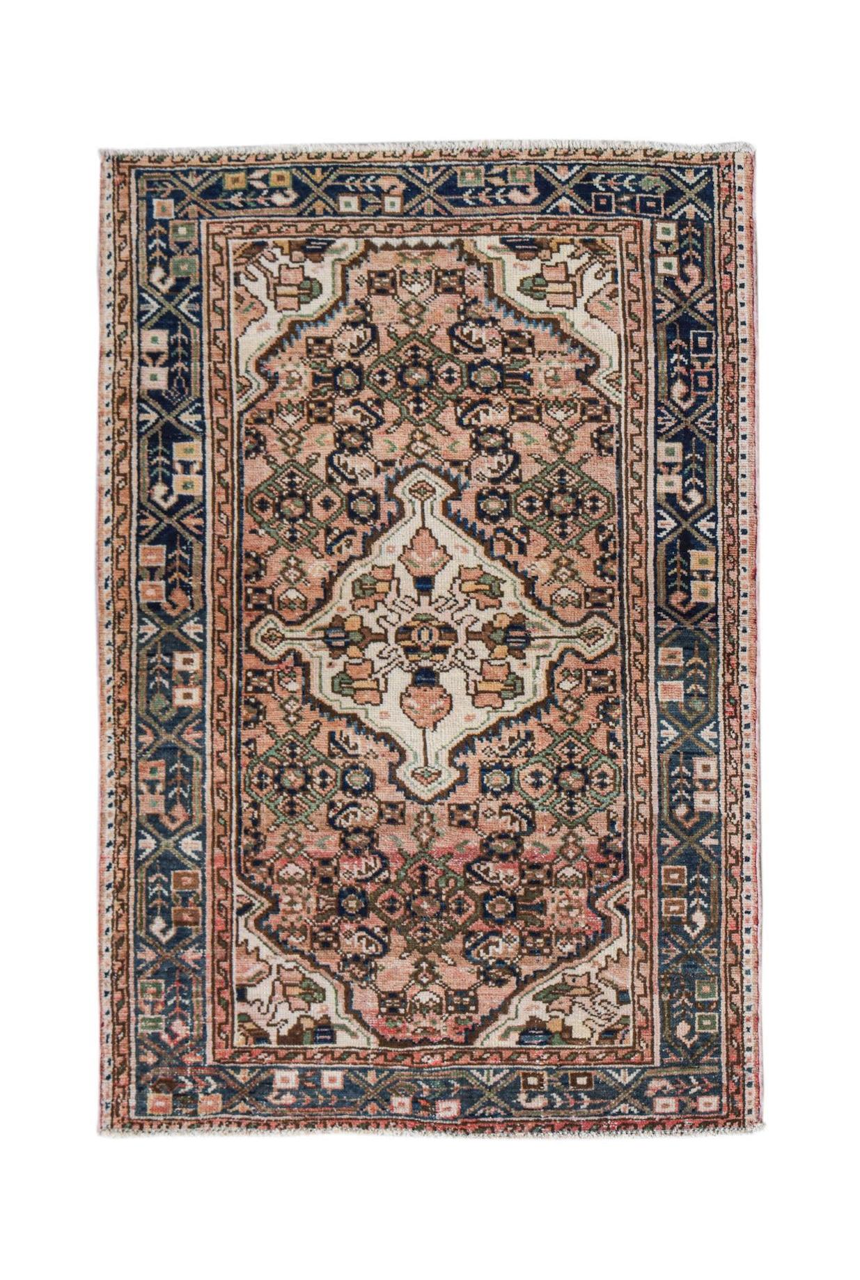 A handwoven vintage Persian rug featuring a central medallion in shades of pink, blue, and cream.