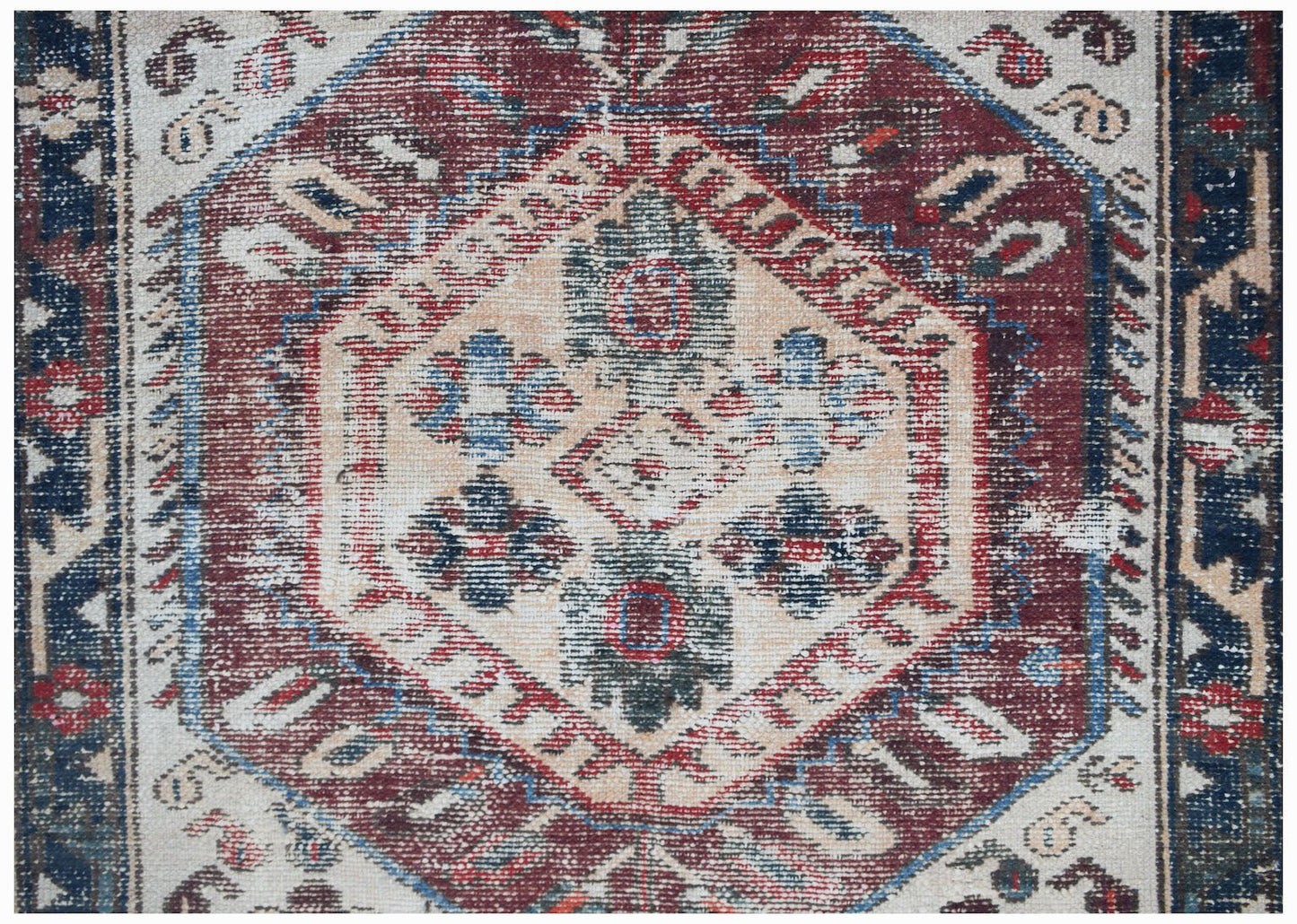 A handwoven vintage Persian rug featuring a central geometric medallion in red, blue, and cream.