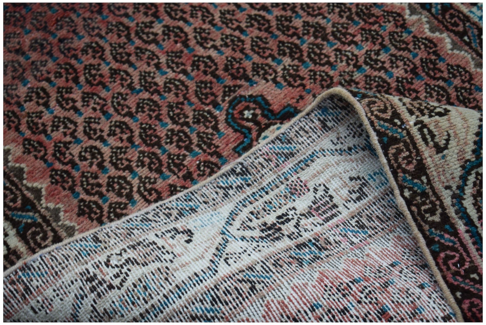 A vintage Persian rug with a repeating dark pattern on a faded red field, shown folded.