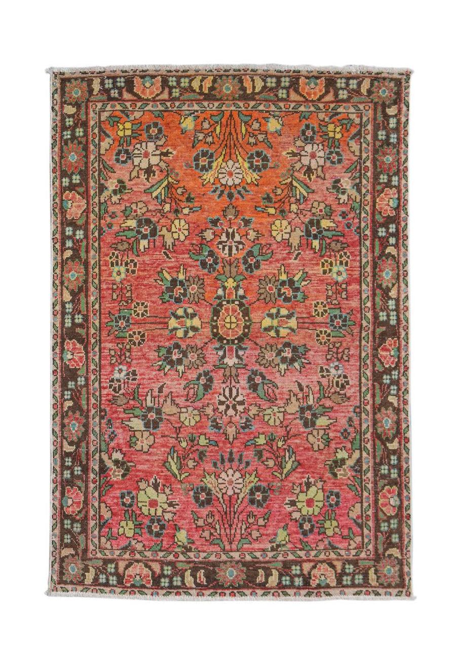 A vintage handwoven Persian rug featuring a floral pattern in shades of red, orange, and brown.