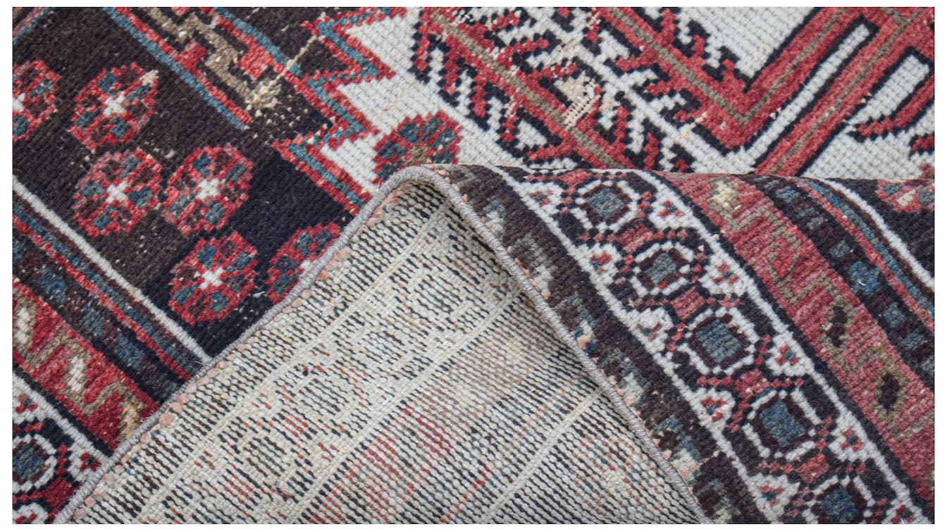A handwoven vintage Persian rug with a geometric pattern in red, blue, and dark brown wool.