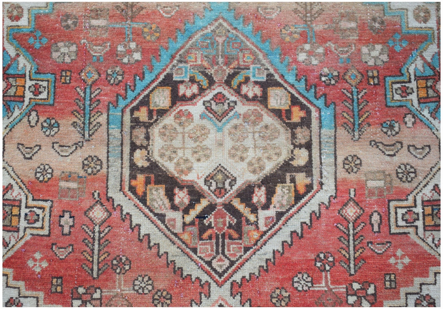 A vintage handwoven Persian rug featuring a central geometric medallion in red, blue, and cream.