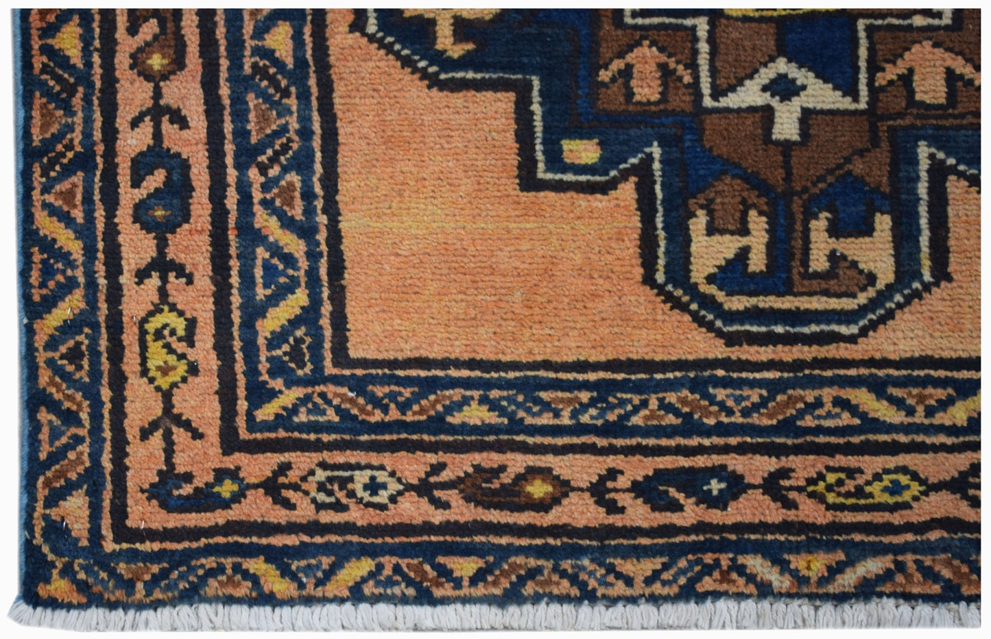 A vintage Persian rug featuring a geometric blue and brown pattern on a peach background.