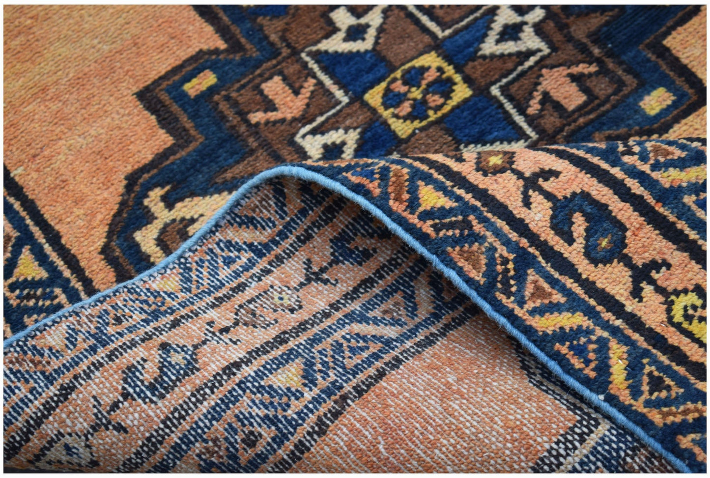 A handwoven vintage Persian rug featuring a geometric pattern in orange, blue, and brown tones.