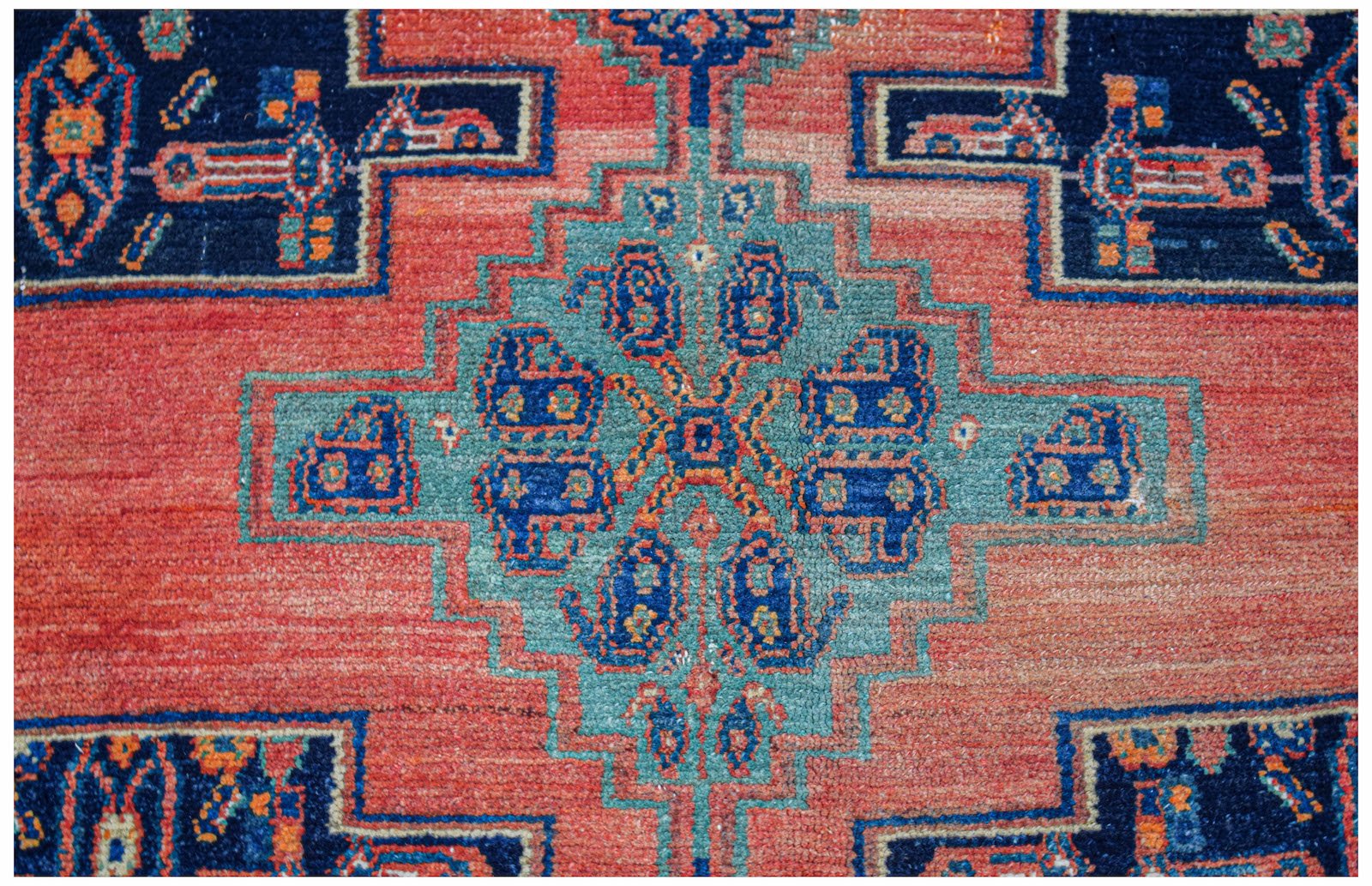 A vintage handwoven Persian rug featuring a geometric blue and teal medallion on a red field.